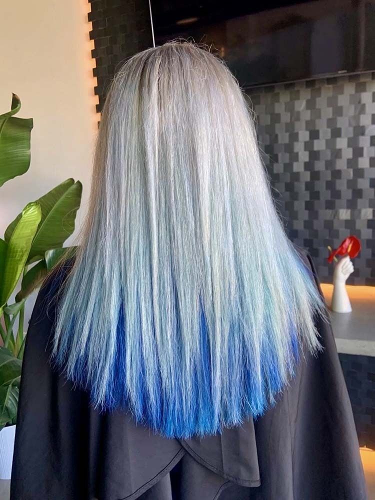 Woman with silver hair fading to blue tips, in a salon setting.