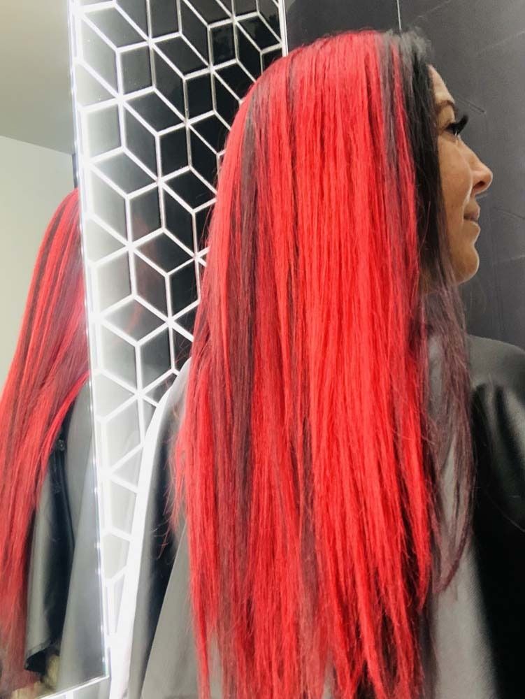 Woman with long red and black hair, in front of a mirror with a geometric design.