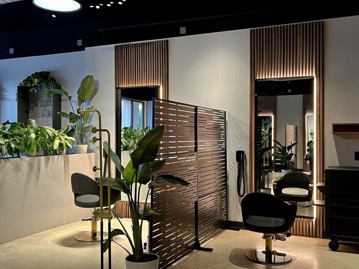 Hair salon interior with mirrors, chairs, and plants. Brown and gold tones, modern design.