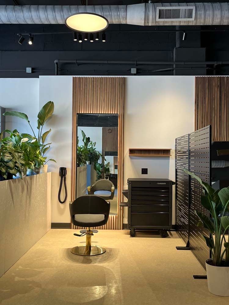 Hair salon interior with chair, mirror, wooden paneling, and plants.