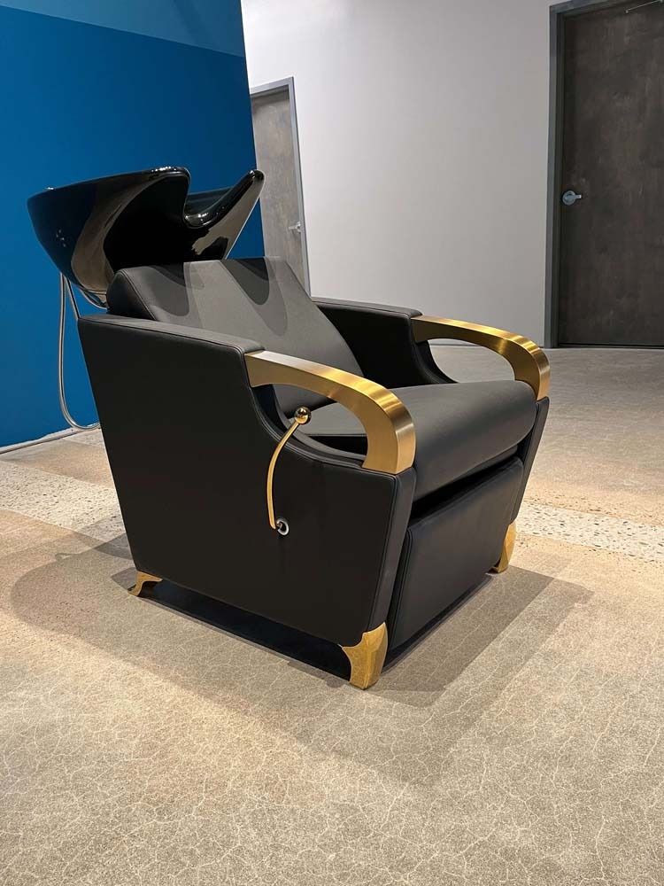 Black salon chair with gold accents and a shampoo bowl.
