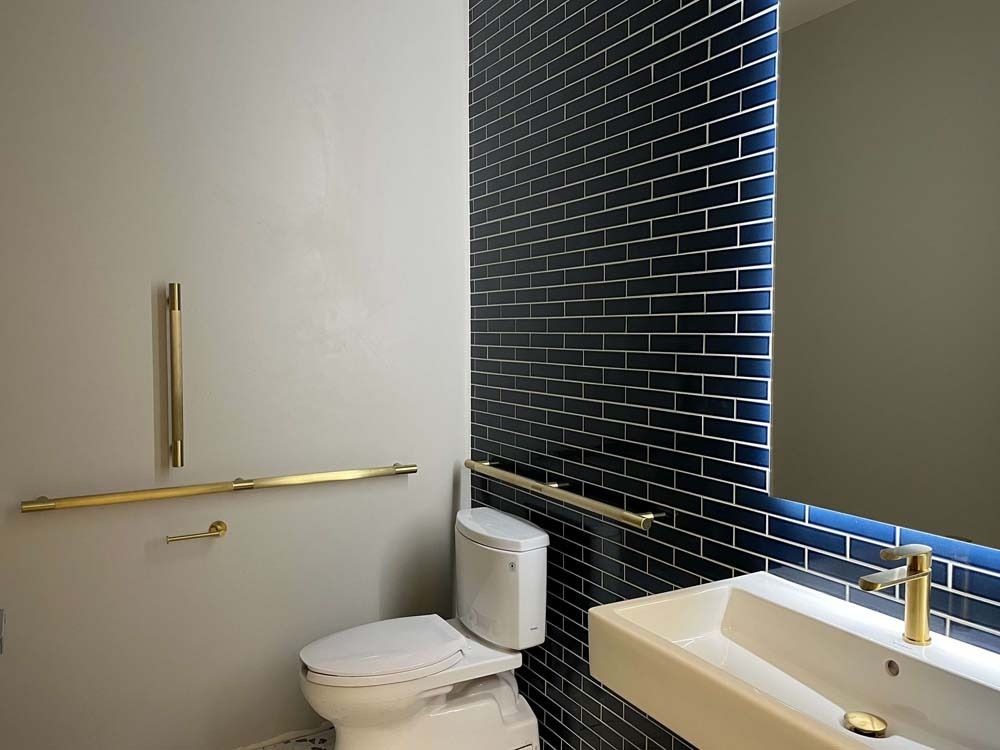 A modern bathroom with a white toilet, sink, and dark blue tile wall with gold fixtures.