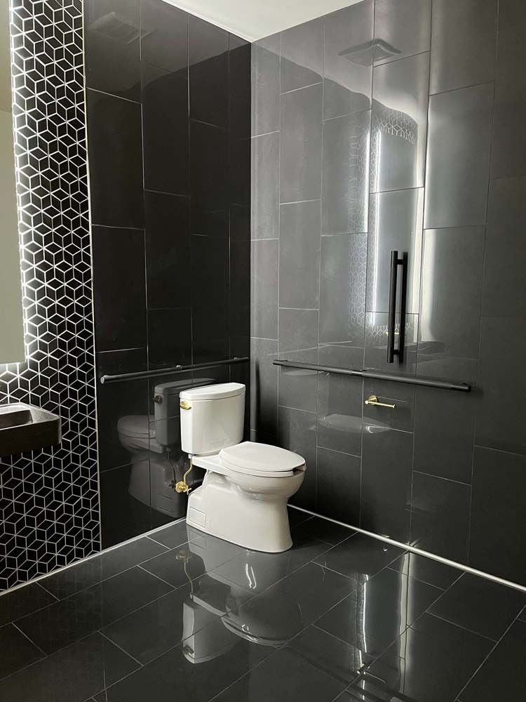 Dark tiled bathroom with toilet and grab bars for accessibility.
