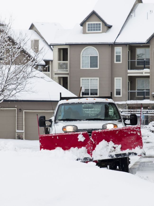 a red snow plow is clearing snow in front of a house