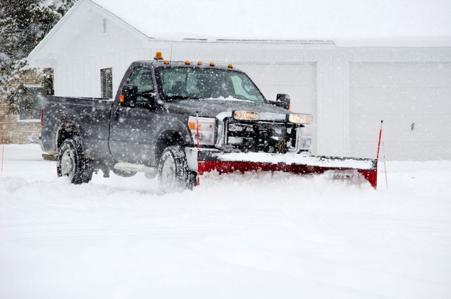 a truck is plowing snow in front of a garage .