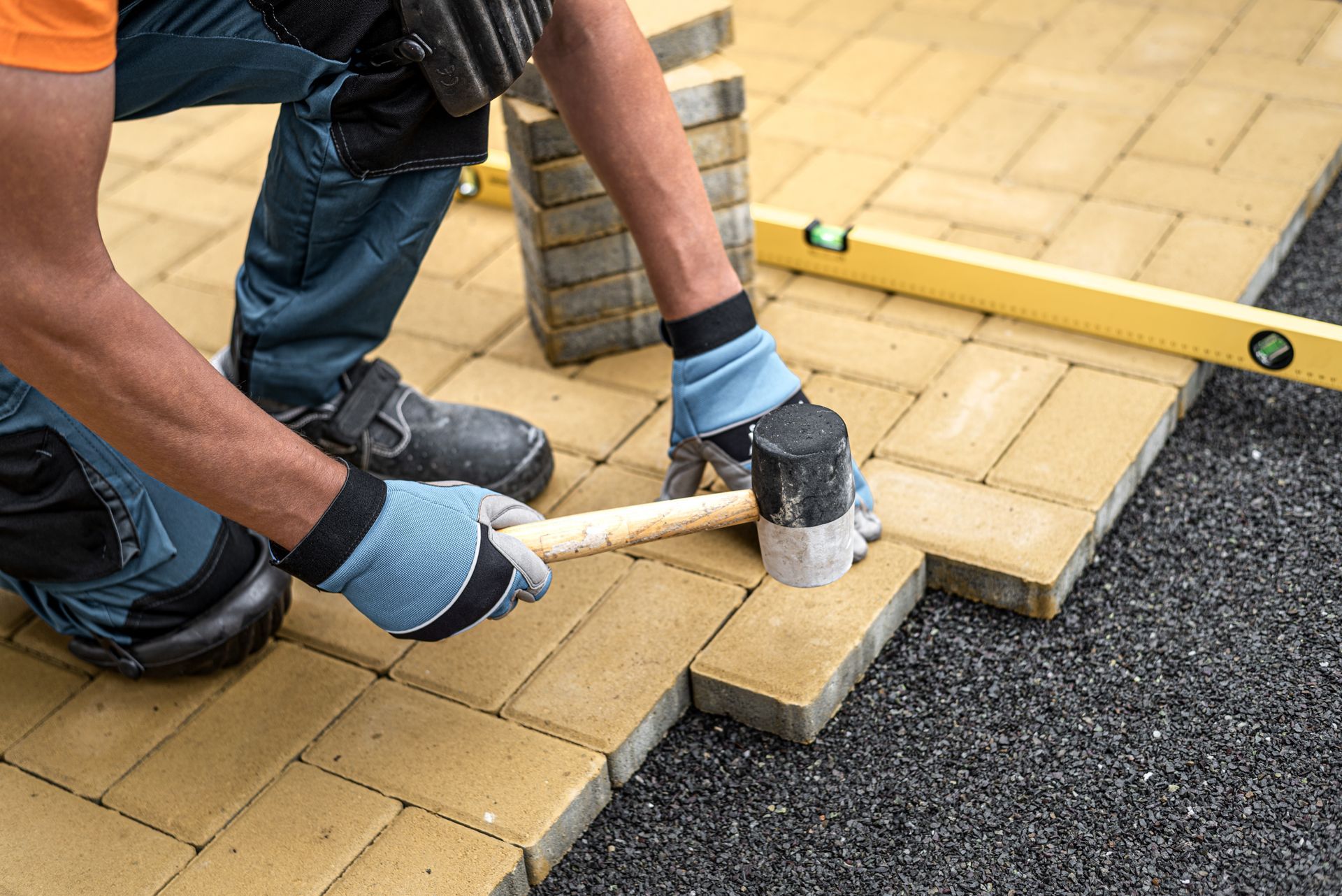 a man is laying bricks on a driveway with a hammer .