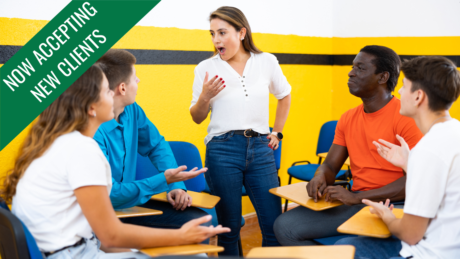 A group of people in a classroom talking. One woman gestures while speaking.