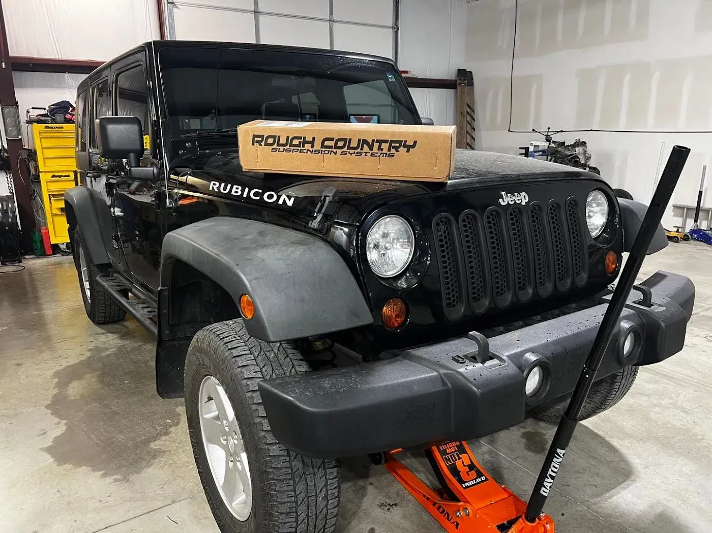Black Jeep Wrangler Rubicon with a Rough Country box on the hood, in a garage setting with an orange jack. | Gearhead Autoworks