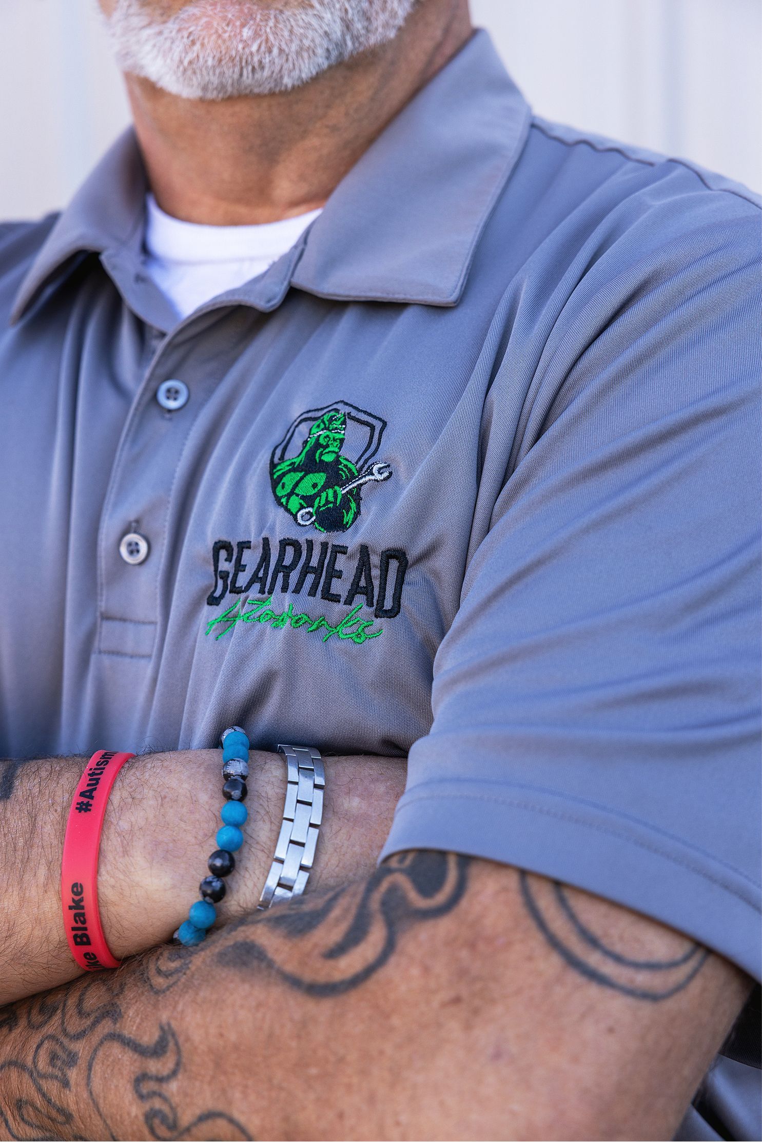 Person with gray shirt and arm tattoo wearing bracelets, logo 
