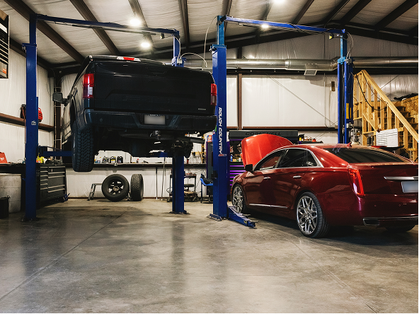 Truck elevated on a lift in a garage, red car with open hood parked nearby. | Gearhead Autoworks