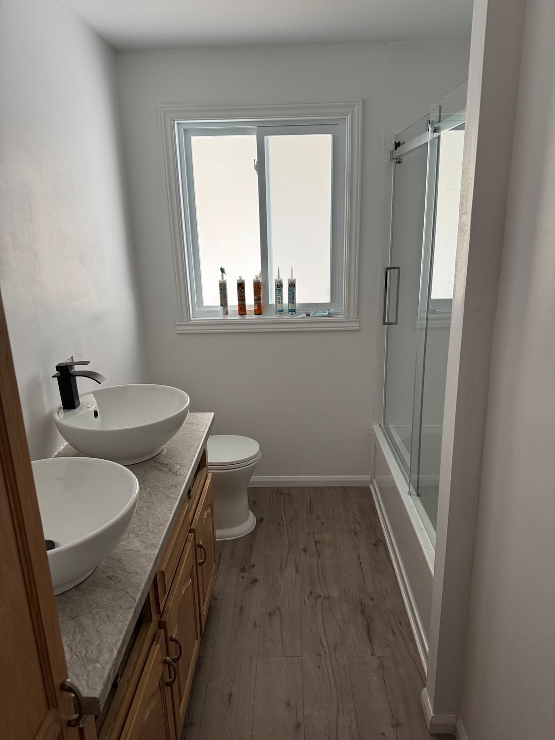 A bathroom with two sinks , a toilet , and a window.