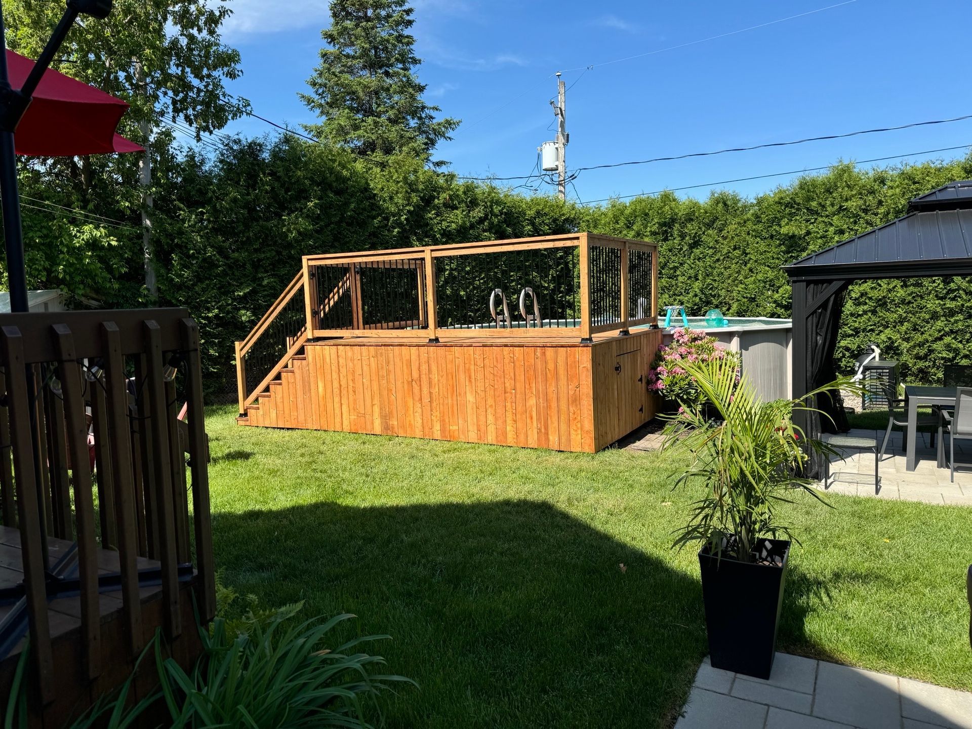 A wooden deck with stairs is in the middle of a lush green yard.