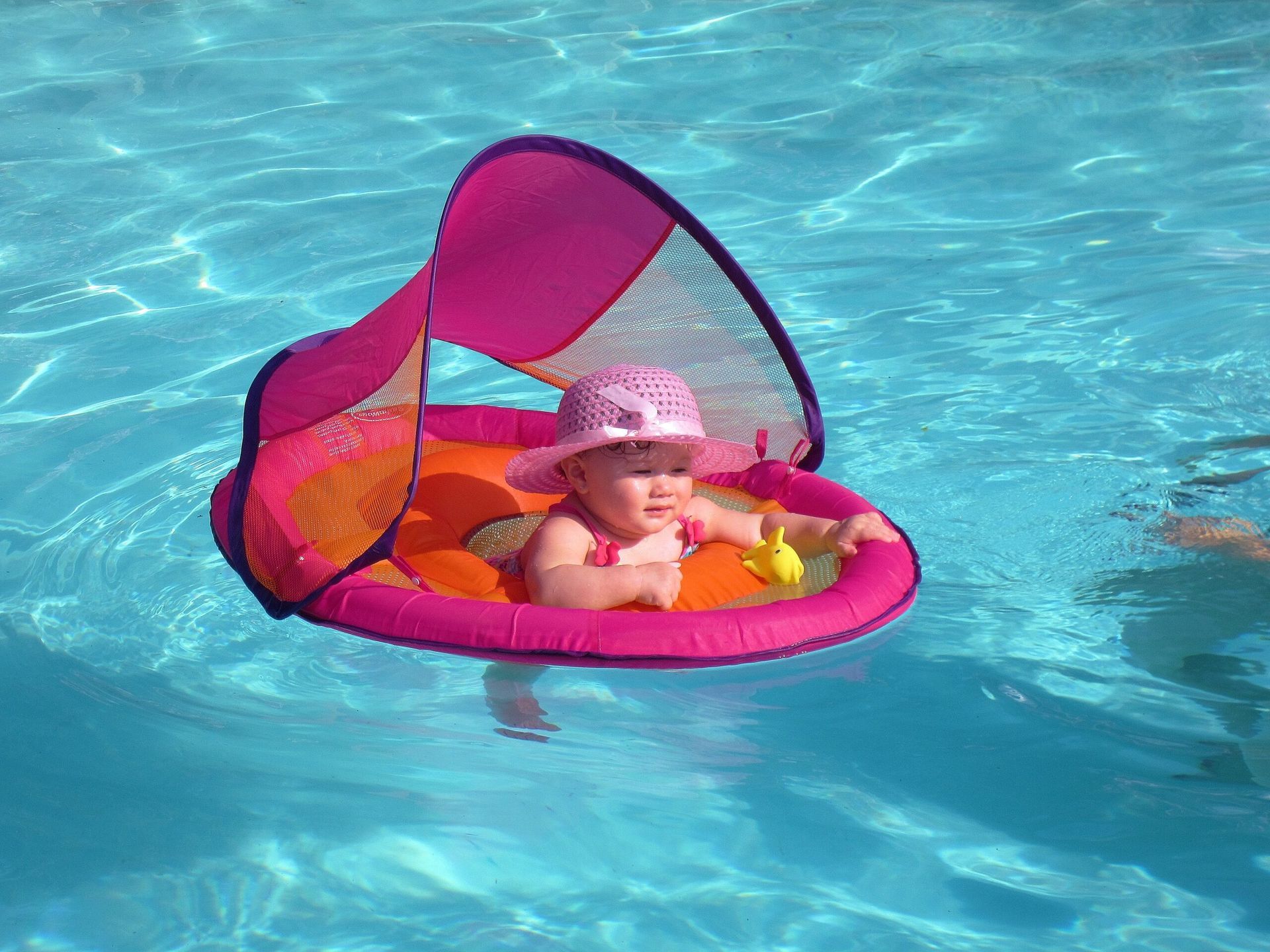 A baby in a pink hat is floating in a pool