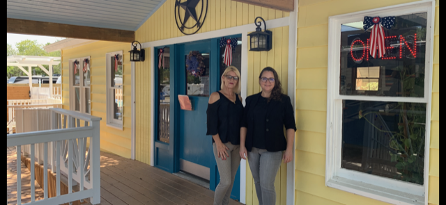 Two women are standing in front of a yellow building.