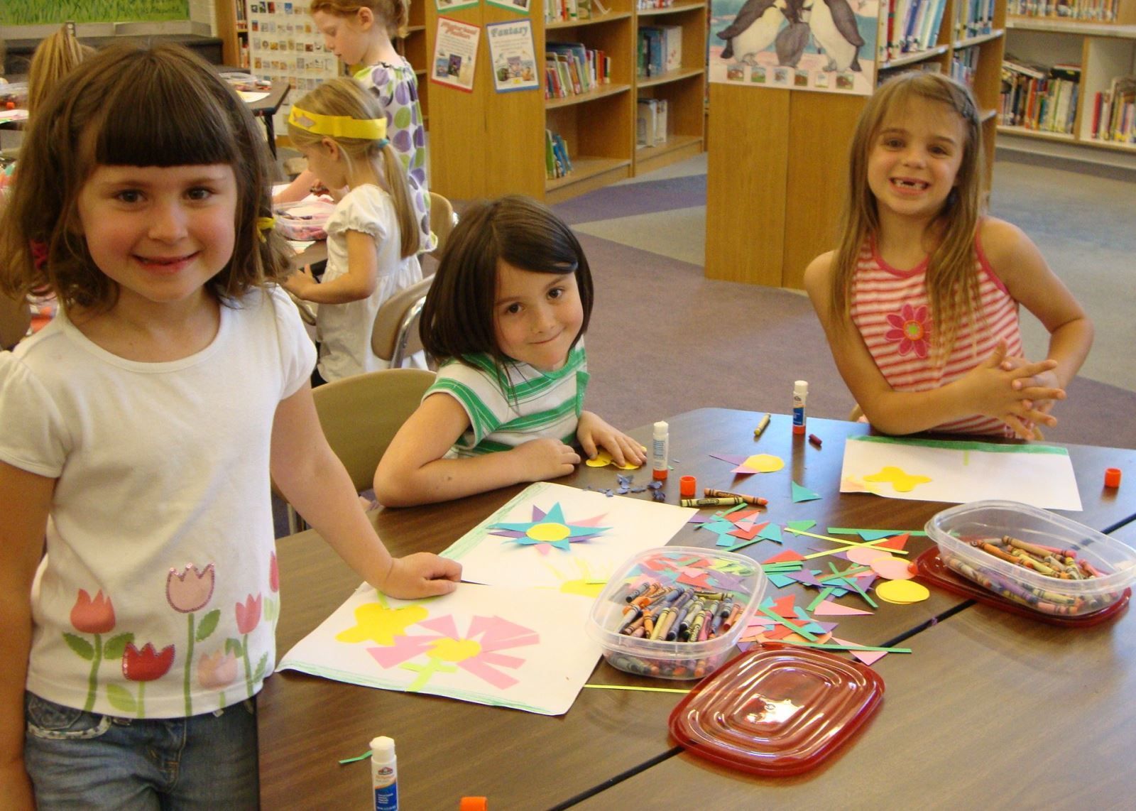 Three little girls are sitting at a table making crafts