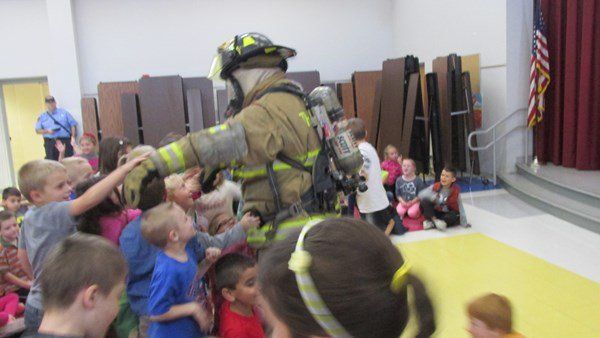 A firefighter is shaking hands with a group of children in a room.