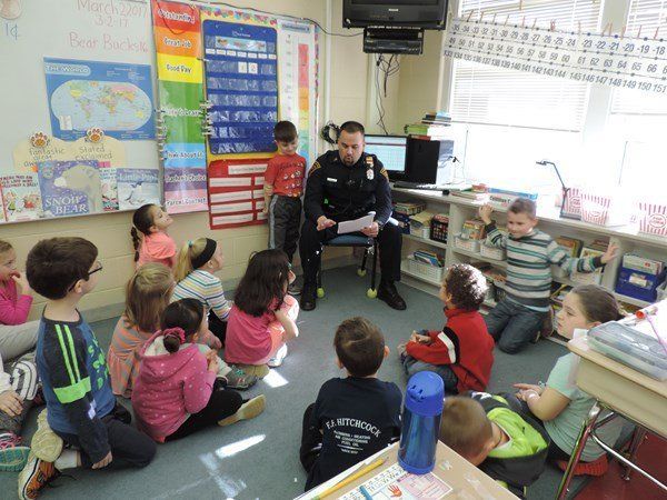 A police officer is reading a book to a group of children in a classroom.