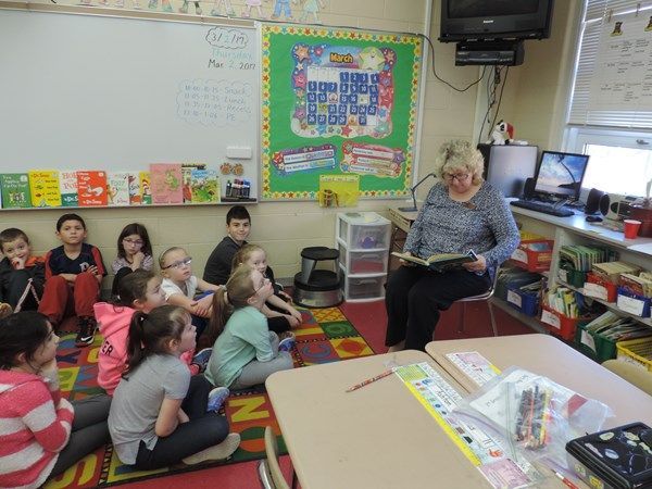 A woman is reading a book to a group of children in a classroom.