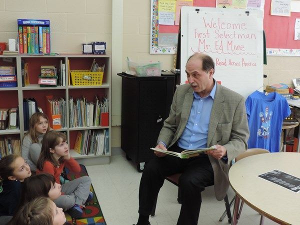 A man is reading a book to a group of children in a classroom