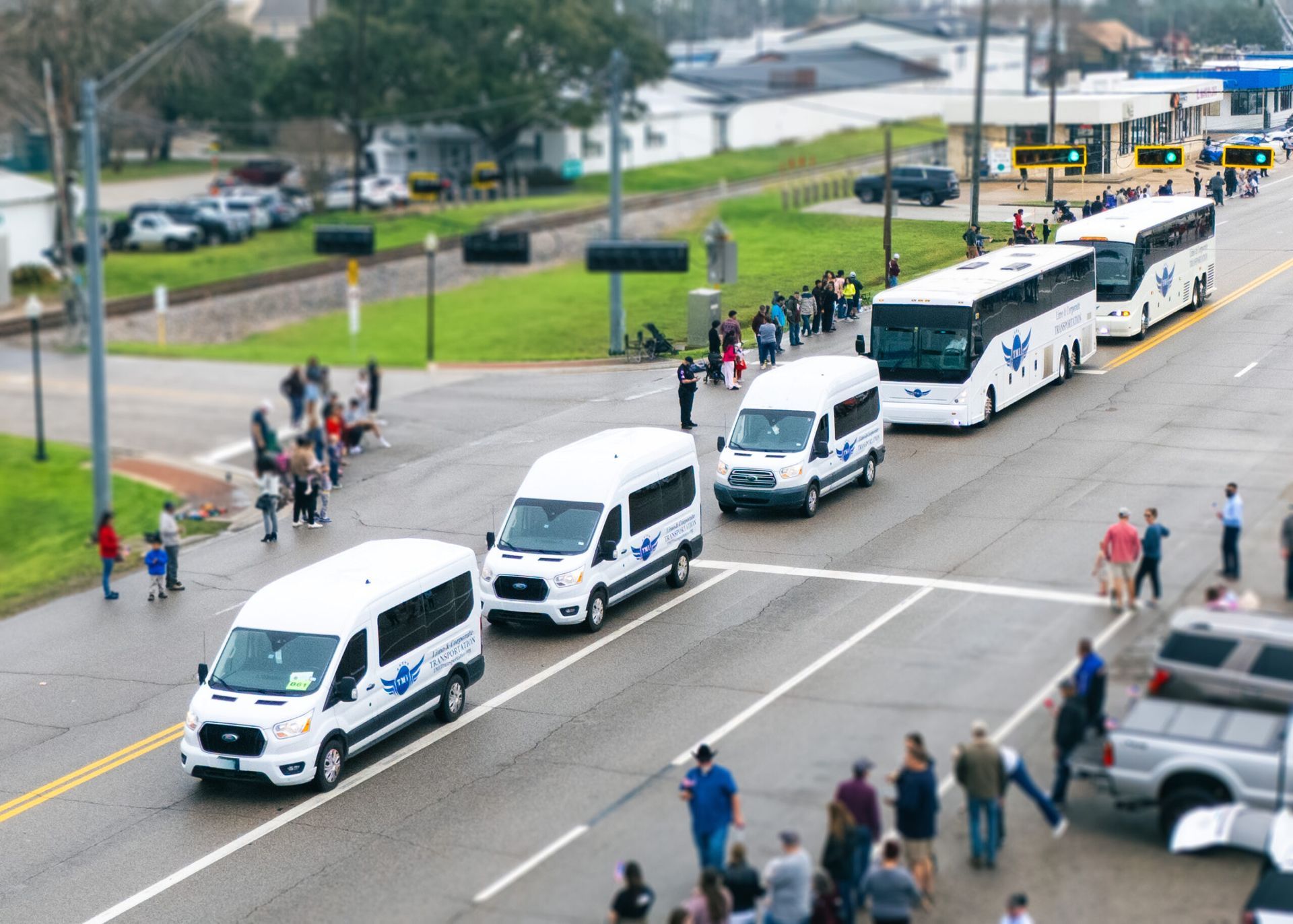 Buses and vans with blue logos parked on a street; people gather alongside the vehicles.