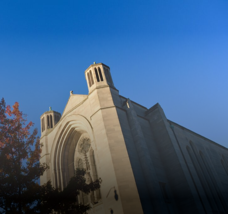 Beige church building against a blue sky, with autumn tree partially in view.