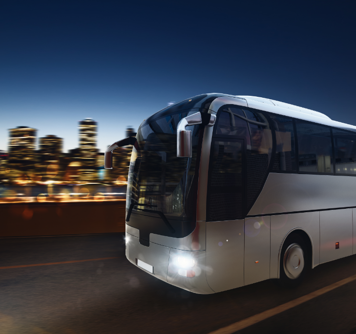 White bus driving on a road at night with city lights in the background.