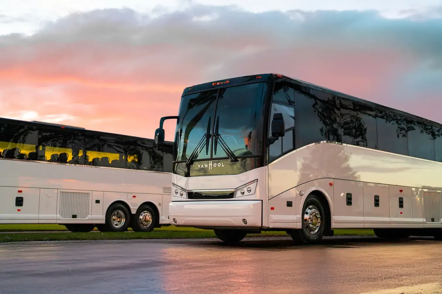 Two white coach buses parked side by side at dusk under a pink and blue sky.