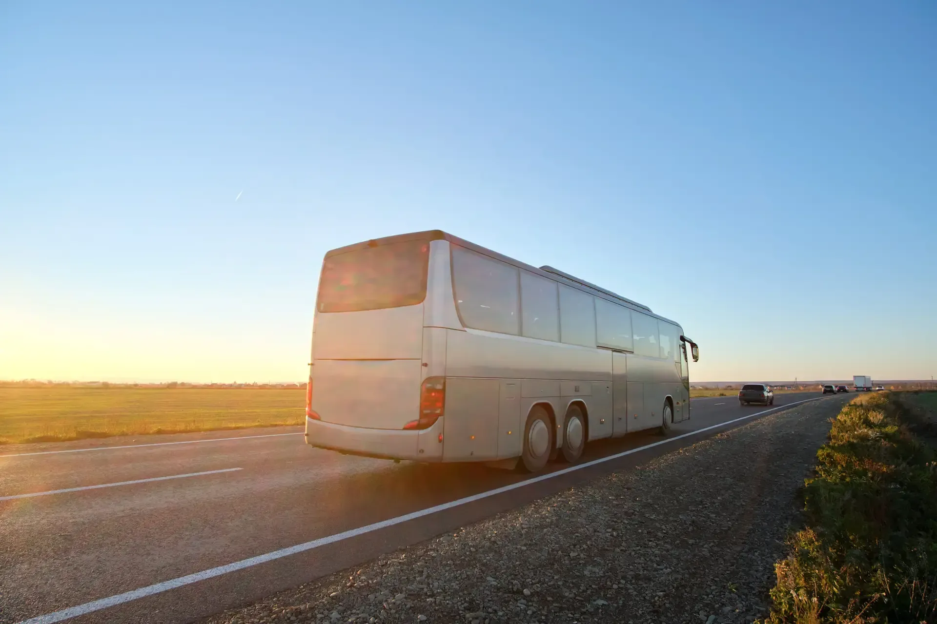 A large white bus traveling on a highway at sunset.
