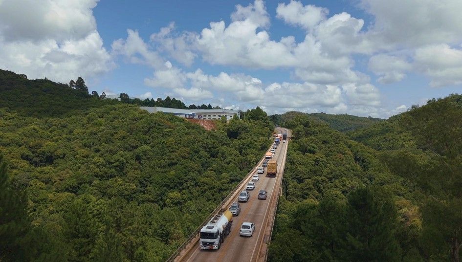 Road winding through green hills with vehicles under a cloudy sky.
