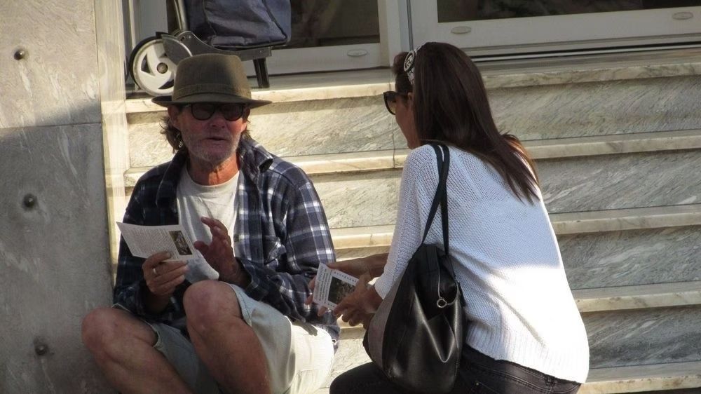 Un homme avec un chapeau est assis sur les marches et parle à une femme.