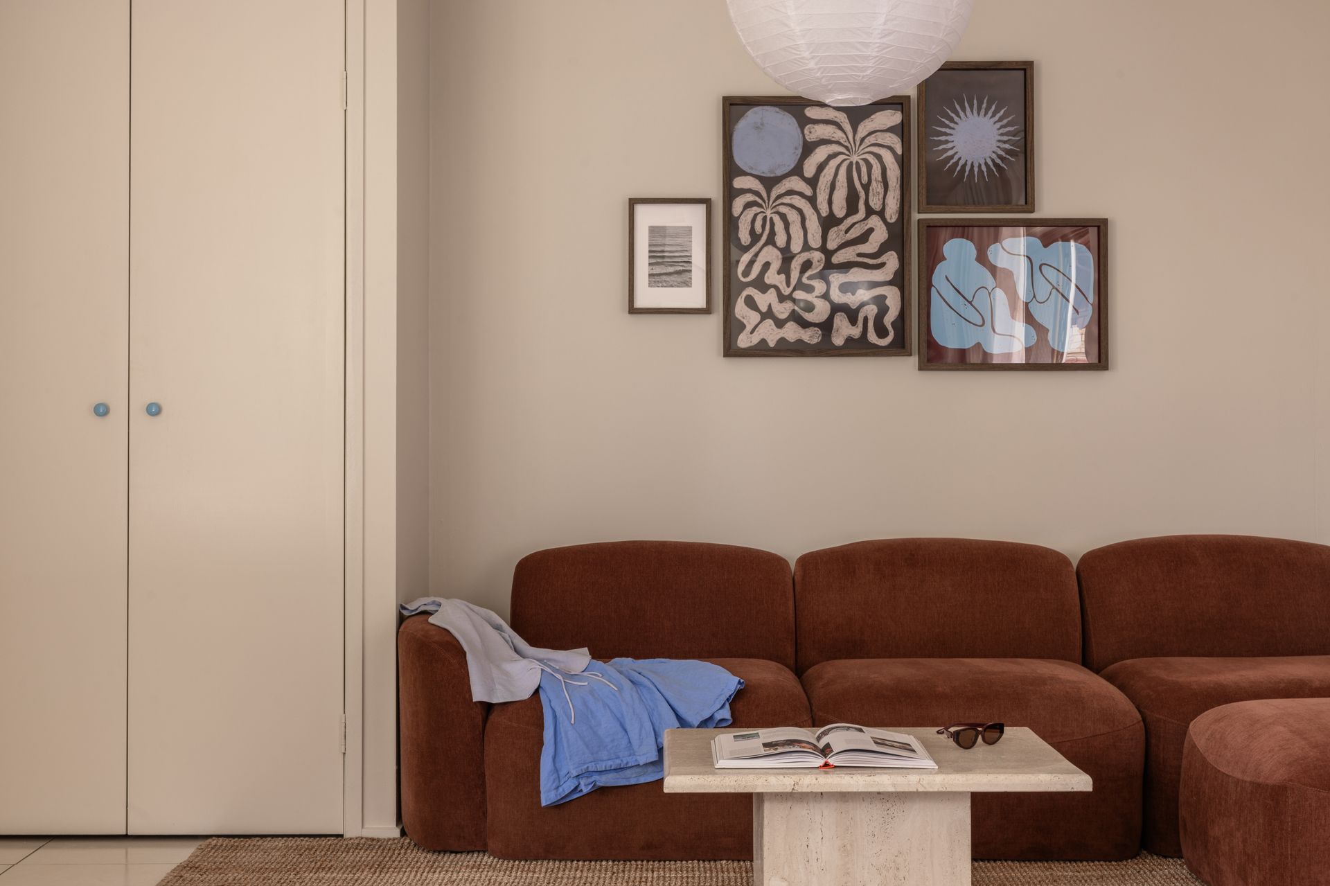 Cozy living room with brown sofa, beige cabinet, framed art, and a lamp over a coffee table.