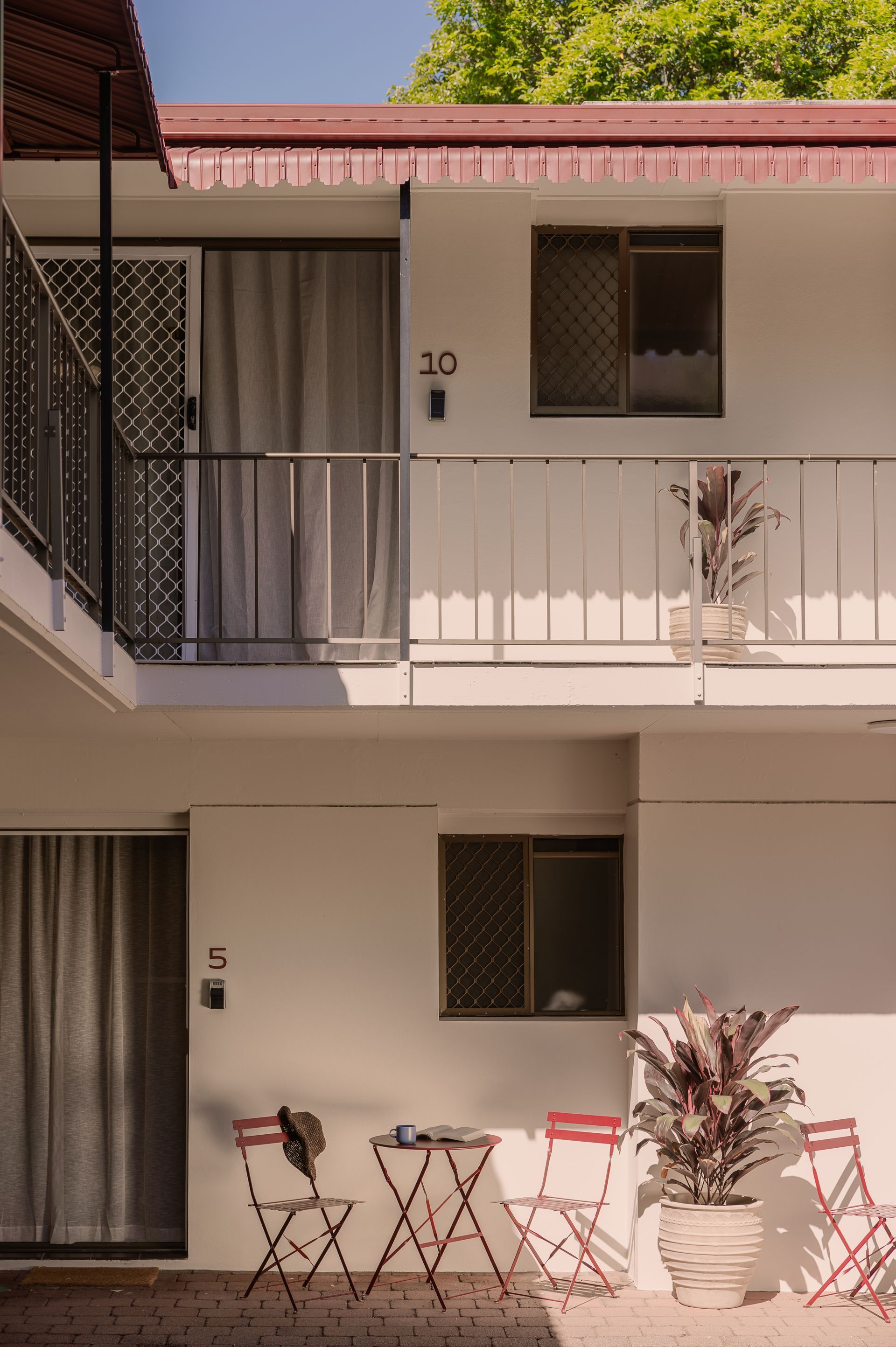 Two-story motel exterior with white walls, red trim, balconies, and patio chairs and tables