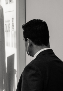 Man in suit stands looking at a wall display, in grayscale.
