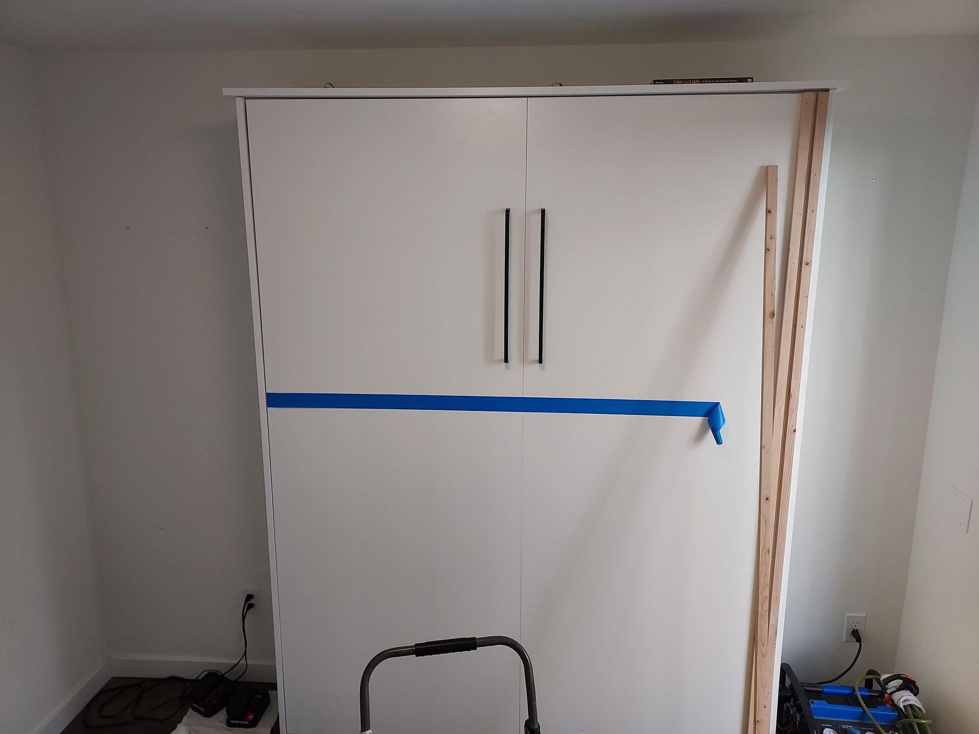 A white cabinet with blue tape on it is being built in a room.