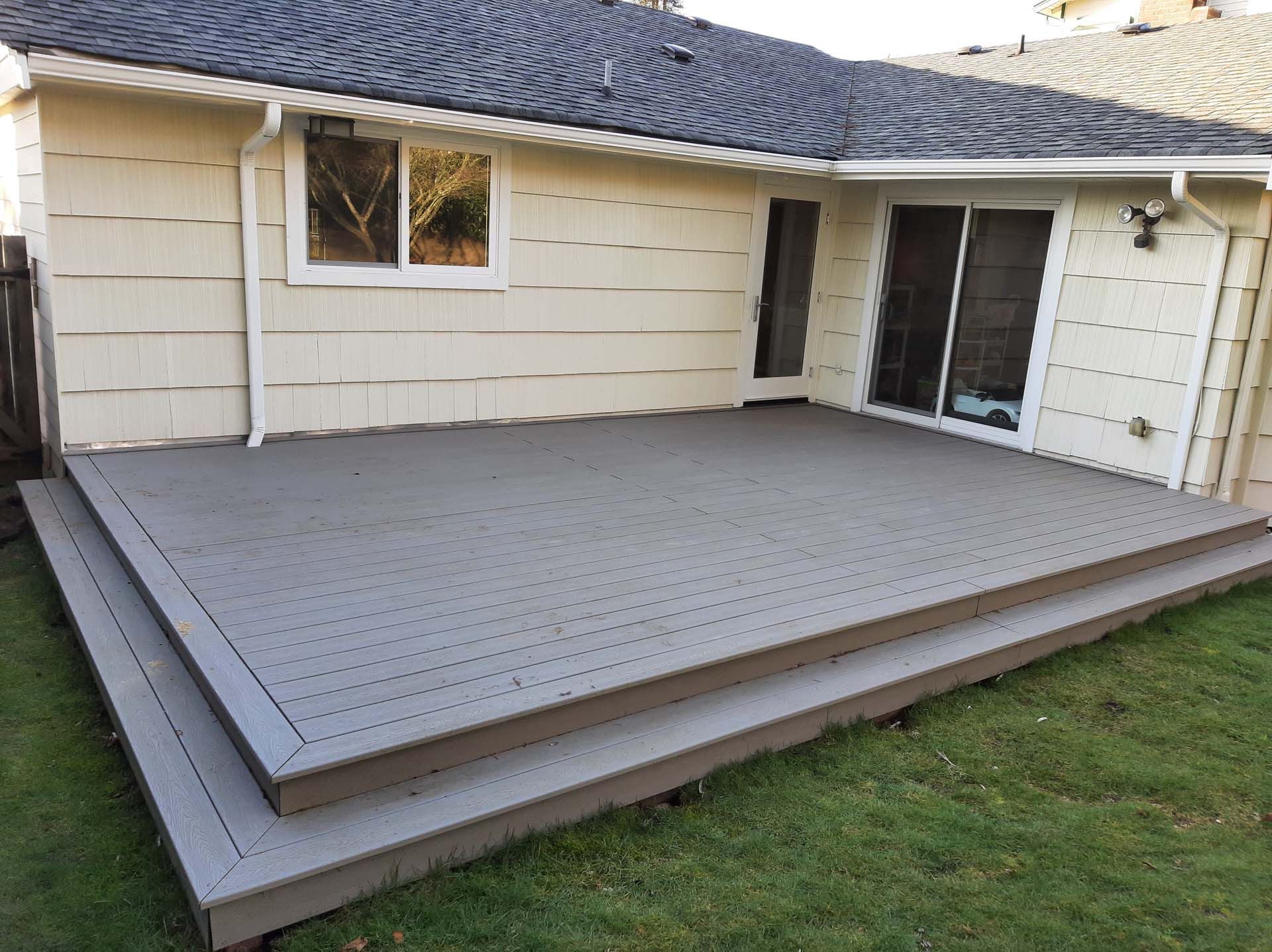 A gray deck is in the backyard of a house.