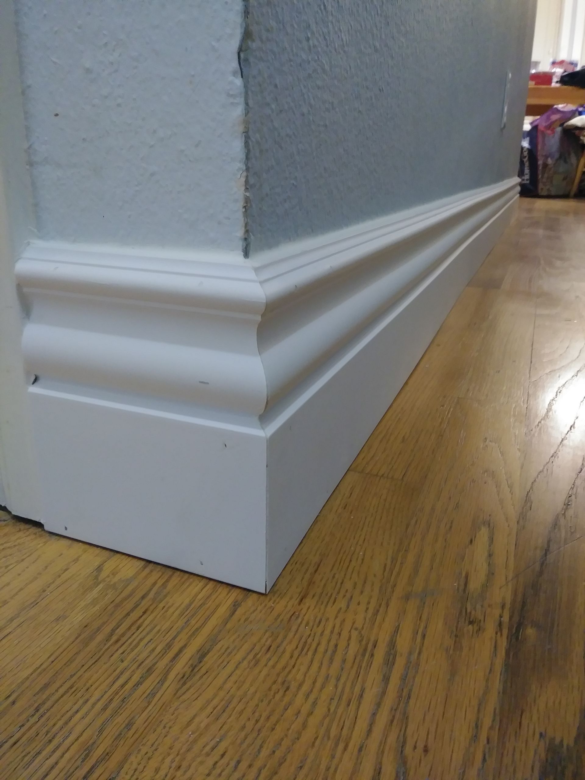 A white molding on a wooden floor next to a wall.