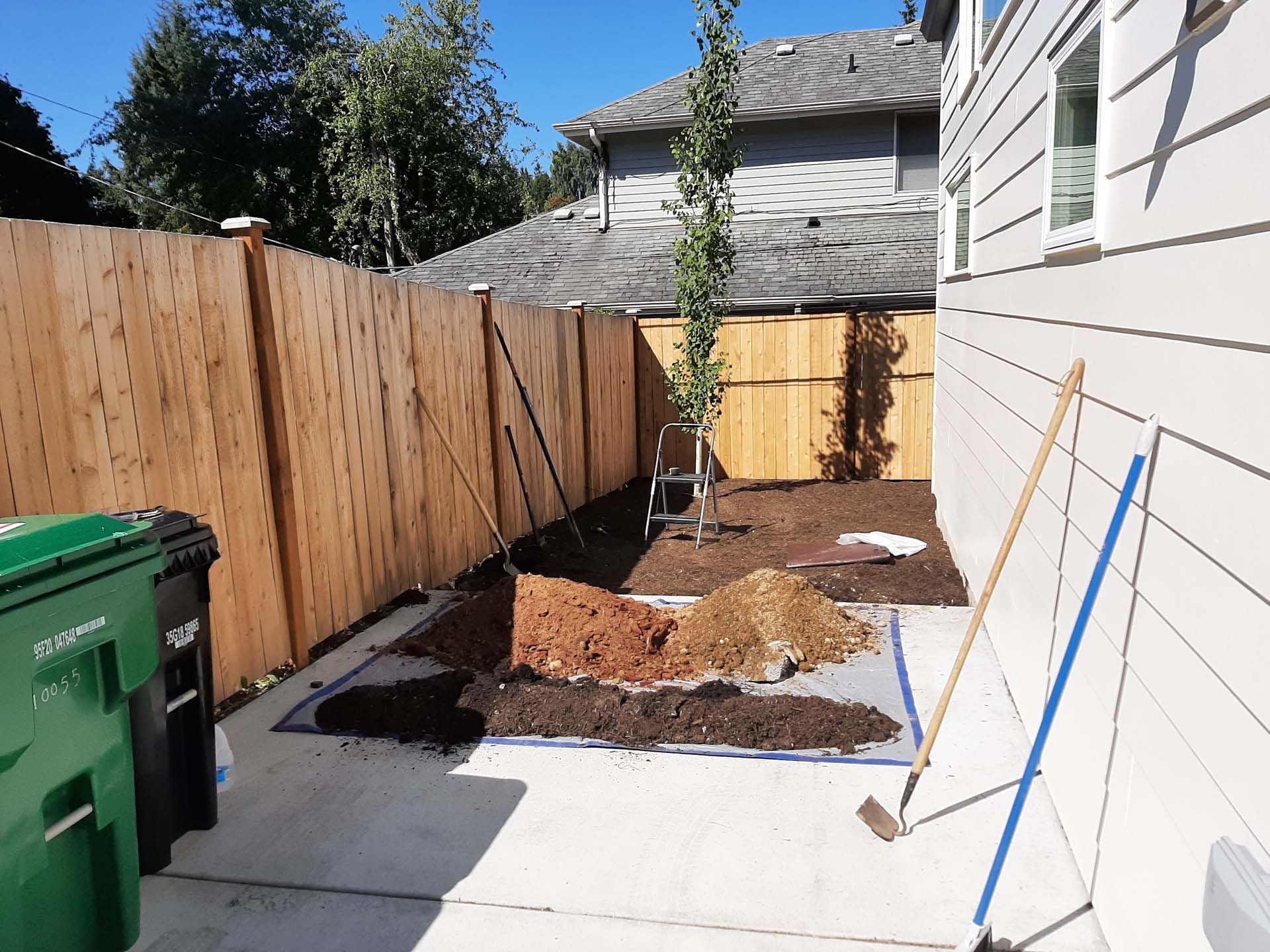 A backyard with a wooden fence and a green trash can