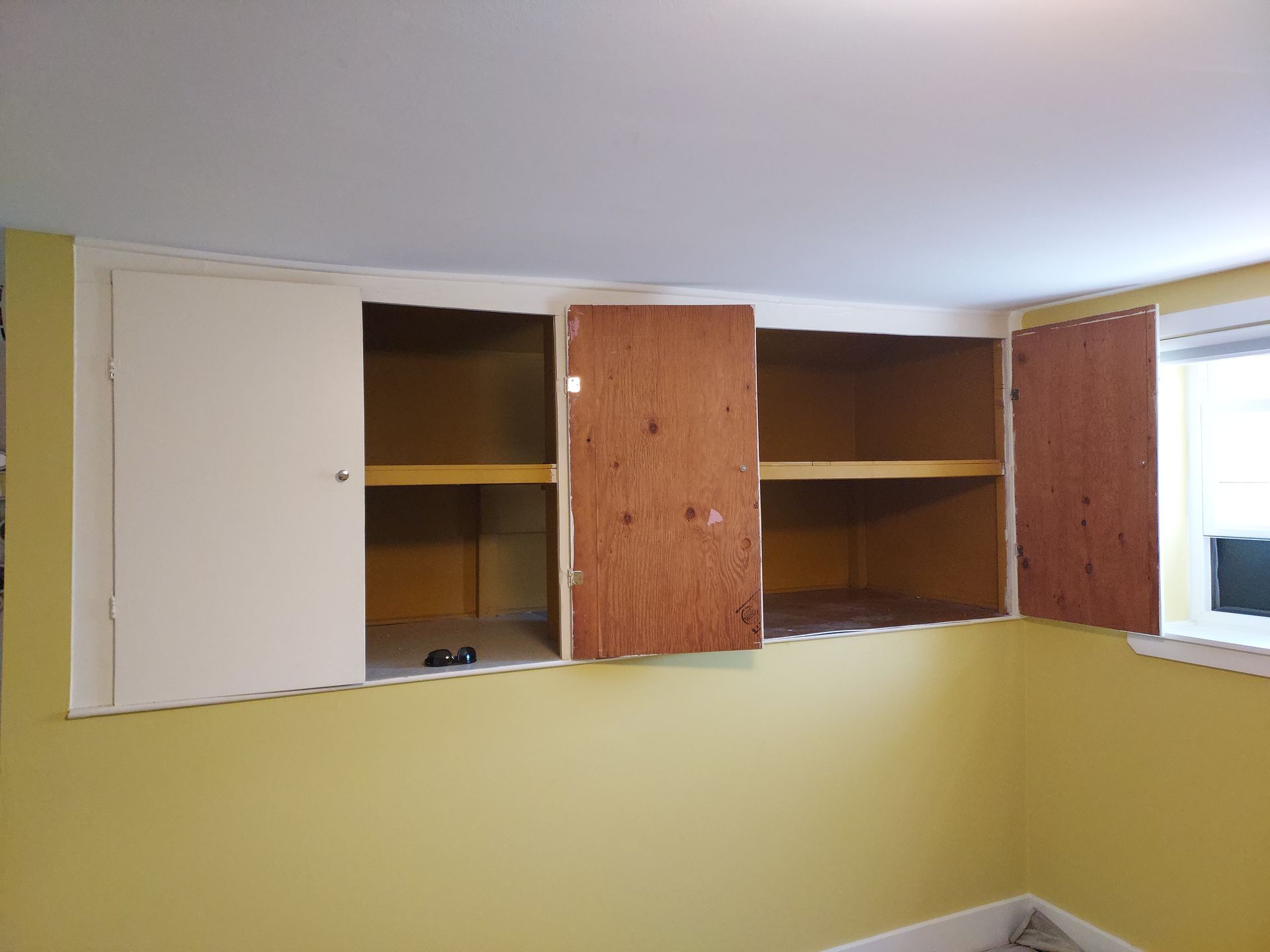A room with yellow walls and wooden cabinets with the doors open