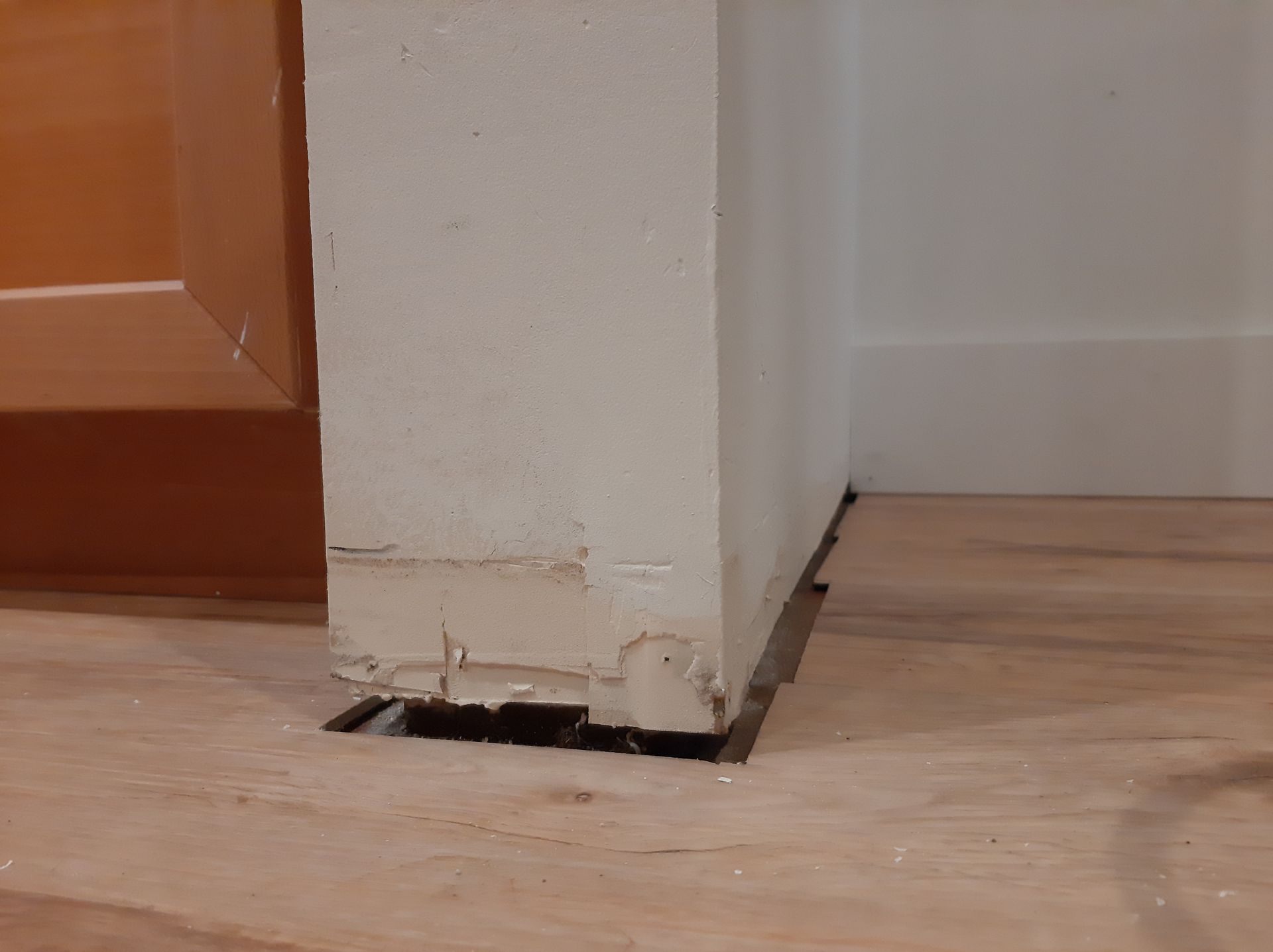 A corner of a wall with a hole in it and a wooden floor.
