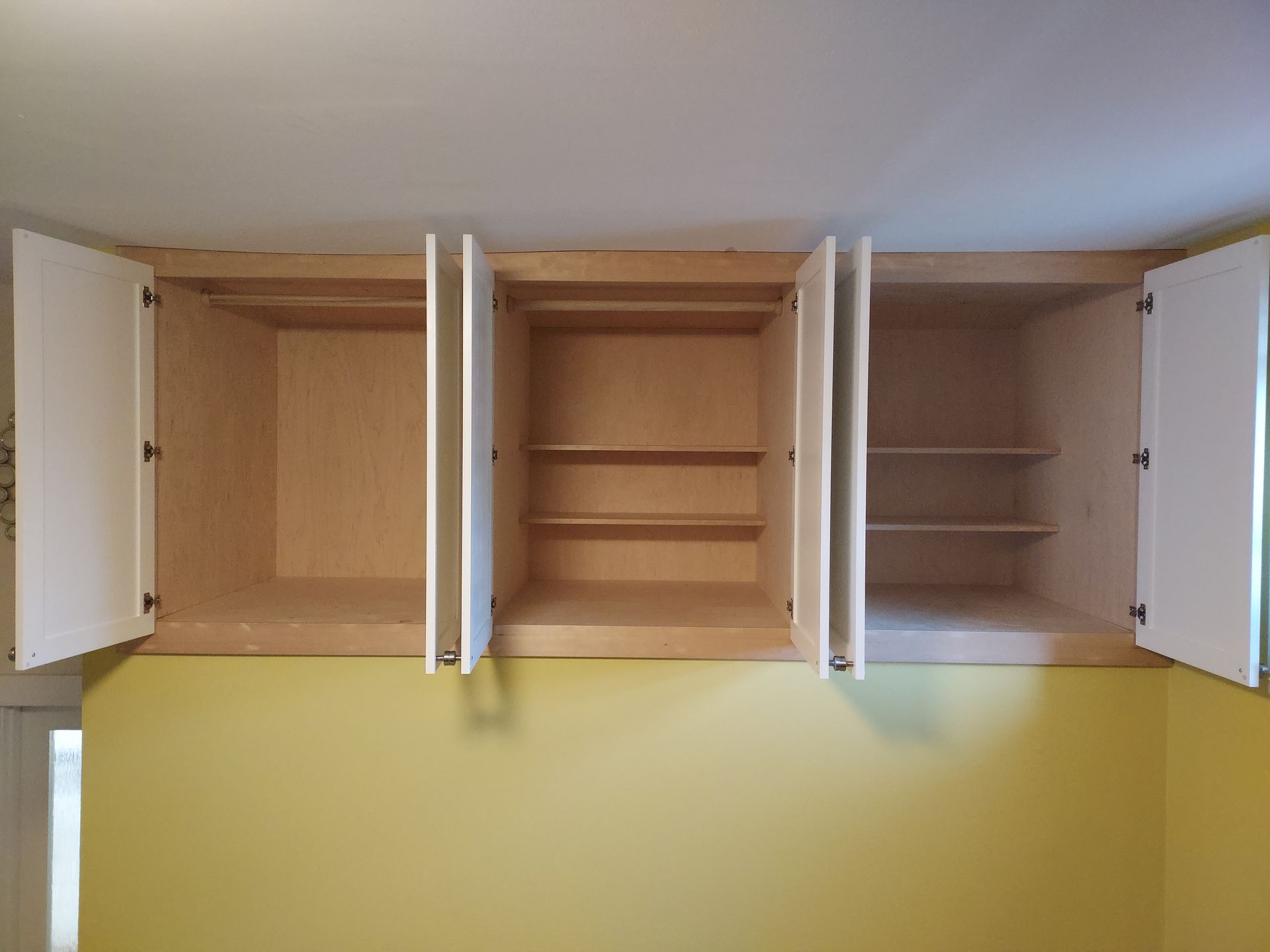 Three empty cabinets are hanging from the ceiling in a room with yellow walls.