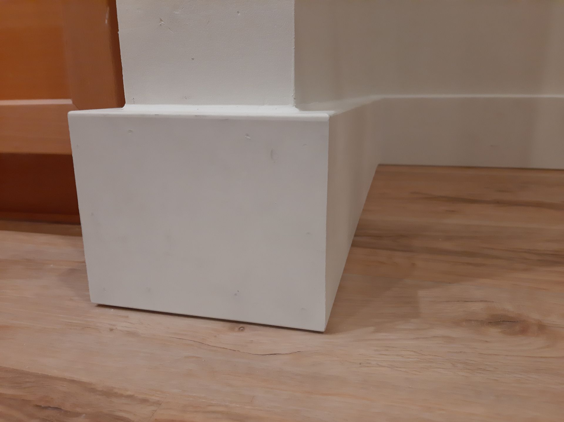 A white block is sitting on a wooden floor next to a wall.