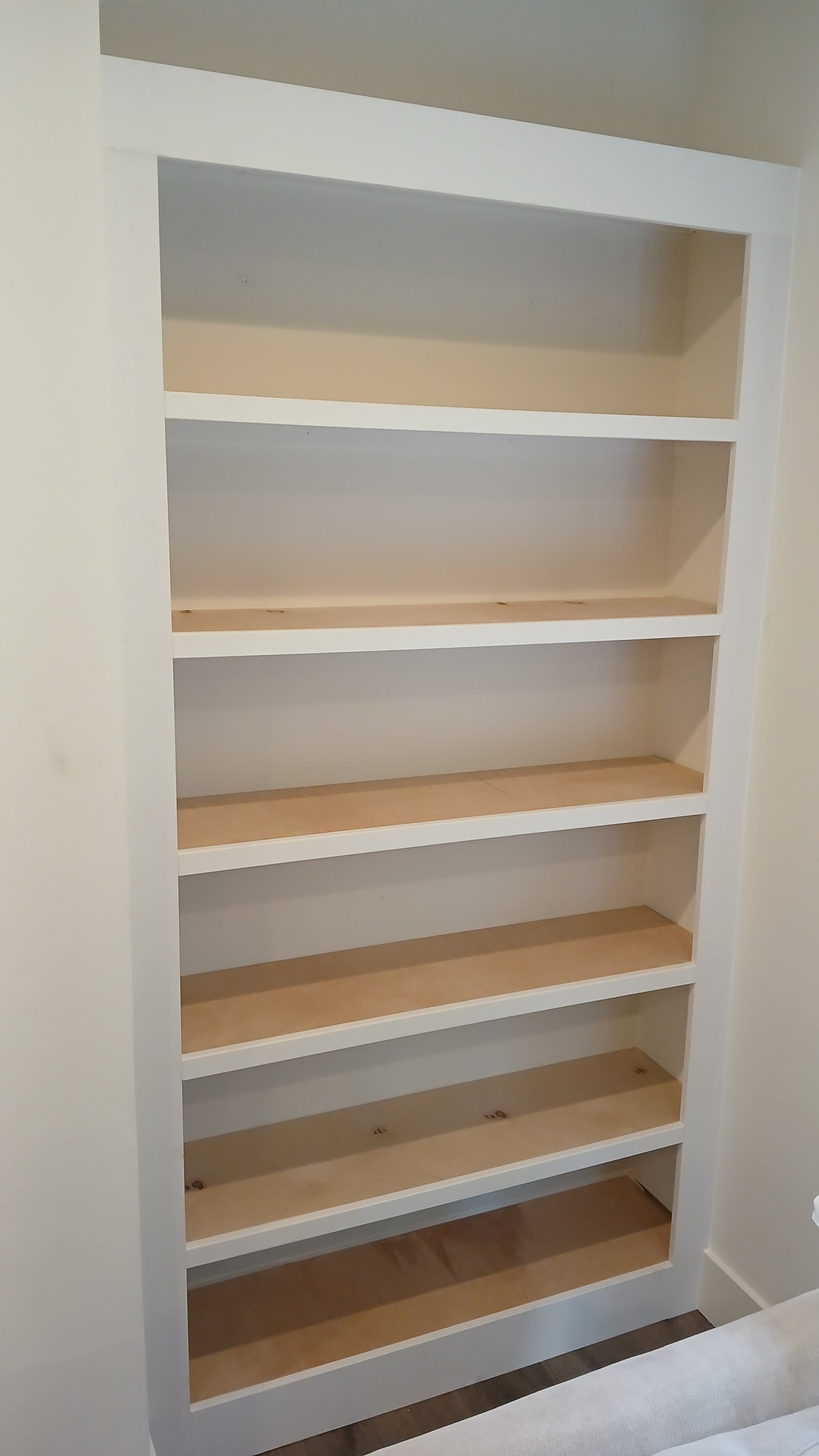 A bookshelf with wooden shelves in a bedroom next to a bed.