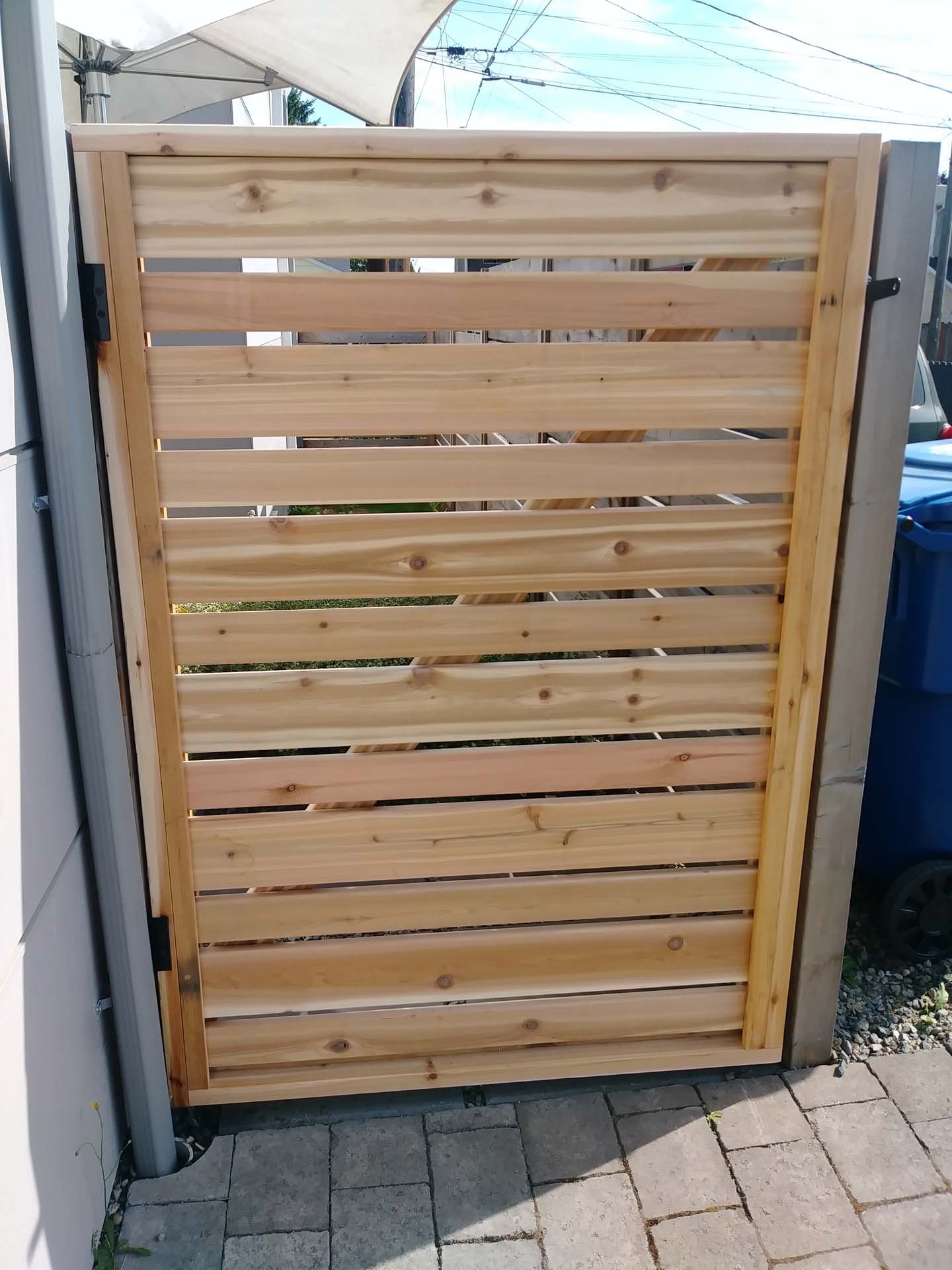 A wooden gate is sitting on a brick sidewalk next to a trash can.