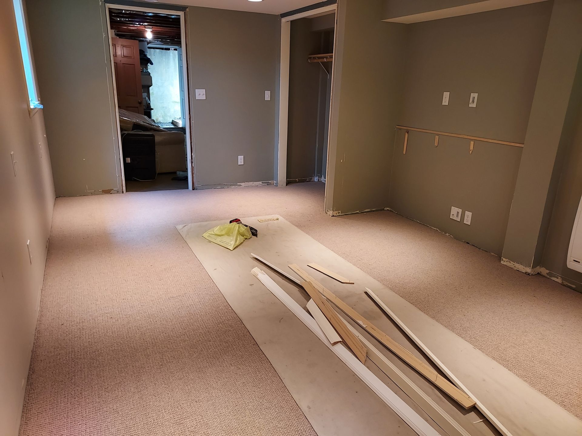 A room with a carpeted floor and a stack of wood on the floor