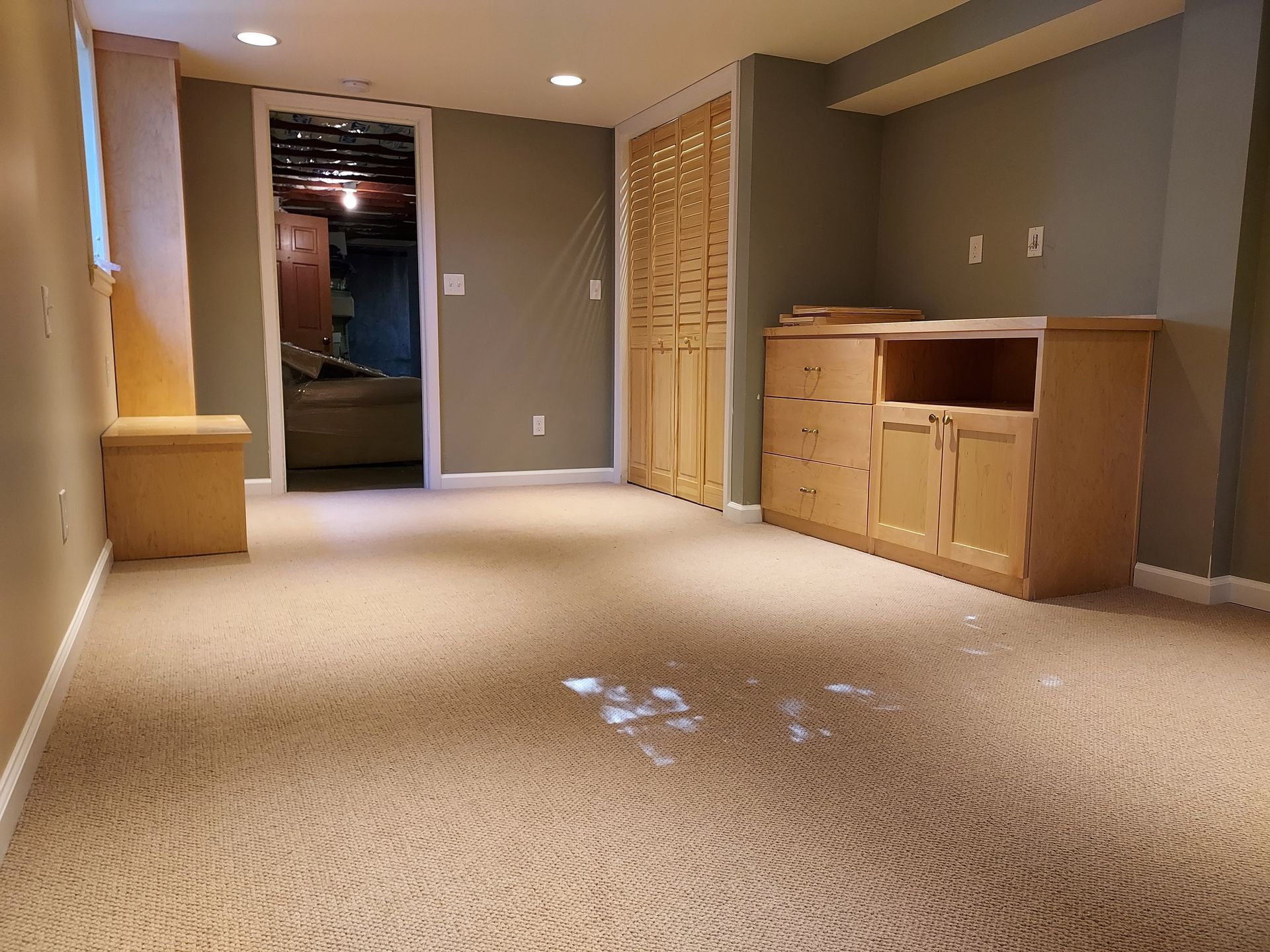 An empty basement with a carpeted floor and wooden cabinets
