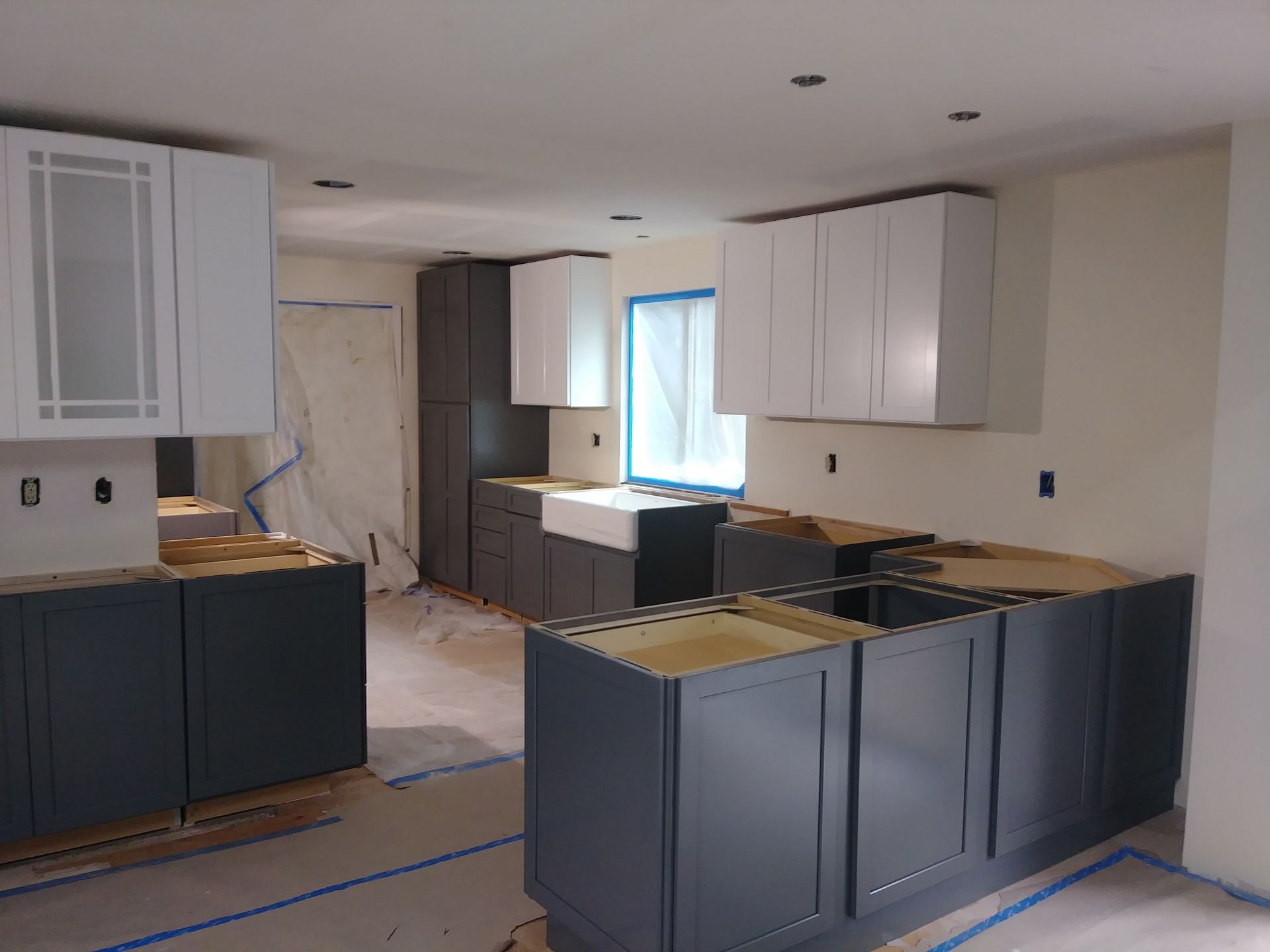 A kitchen under construction with gray cabinets and white cabinets