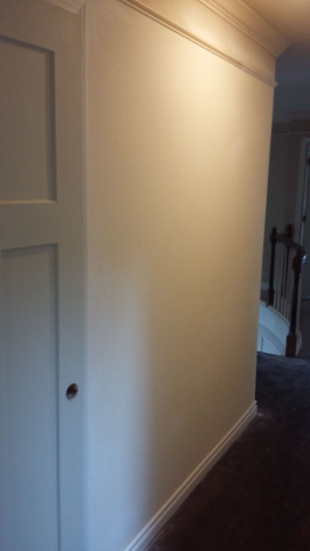 A hallway with a white door and a staircase in the background.
