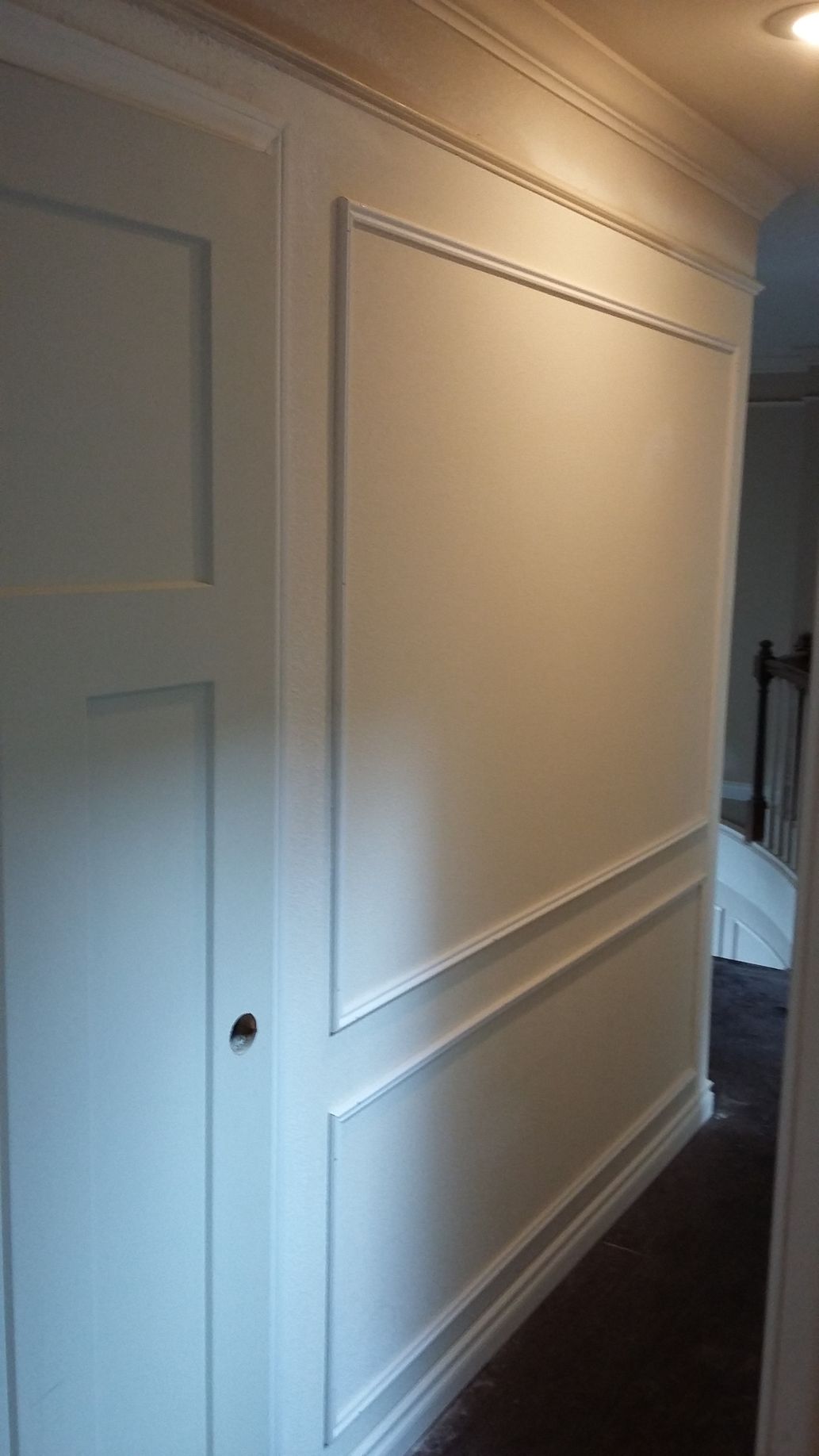 A hallway with white trim on the wall and a door leading to a bedroom.