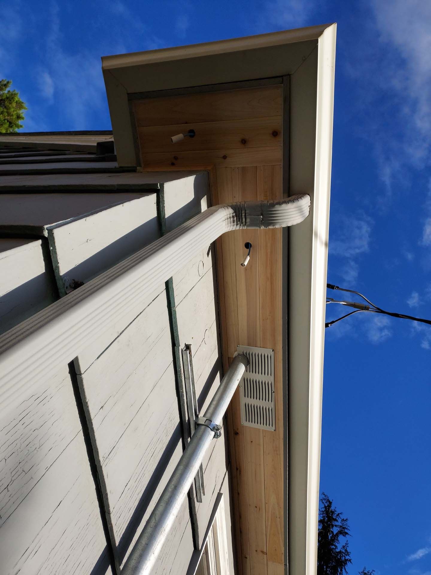 A gutter on the side of a house with a blue sky in the background.
