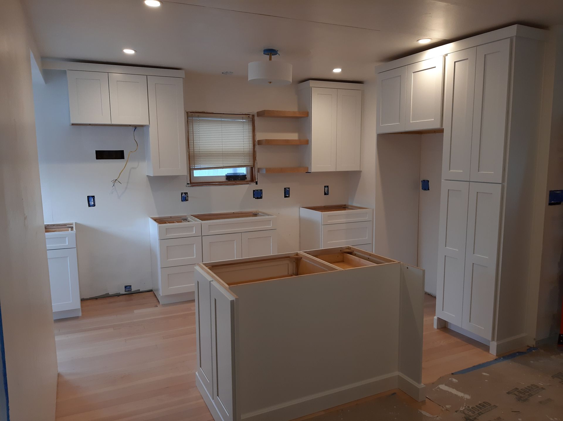 A kitchen under construction with white cabinets and wooden floors